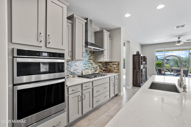 kitchen with wall chimney range hood, a sink, stainless steel appliances, and gray cabinetry