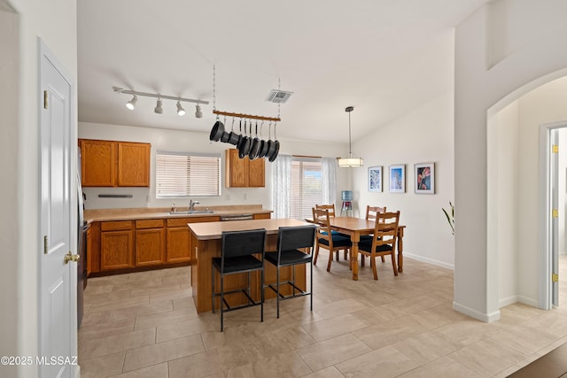 kitchen with lofted ceiling, sink, hanging light fixtures, a kitchen breakfast bar, and a kitchen island