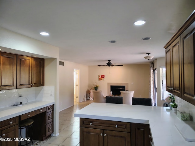 kitchen with tasteful backsplash, a tiled fireplace, open floor plan, a peninsula, and light countertops