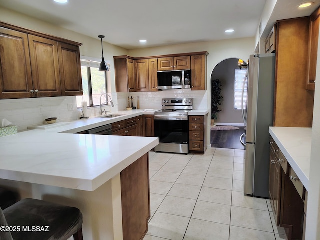 kitchen with light tile patterned floors, arched walkways, a peninsula, stainless steel appliances, and a sink