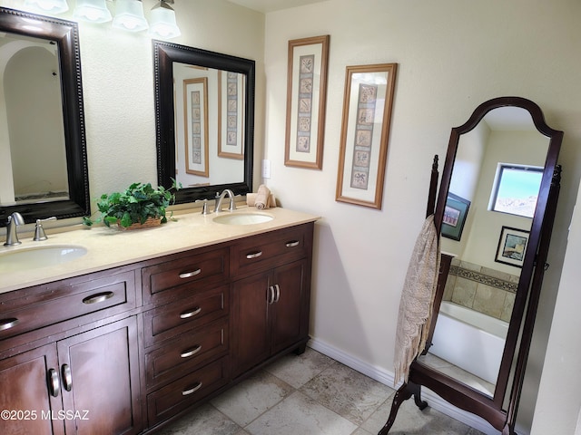 bathroom with double vanity, stone tile floors, baseboards, and a sink