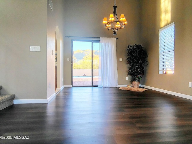 unfurnished dining area with dark wood-type flooring, stairway, a towering ceiling, and baseboards