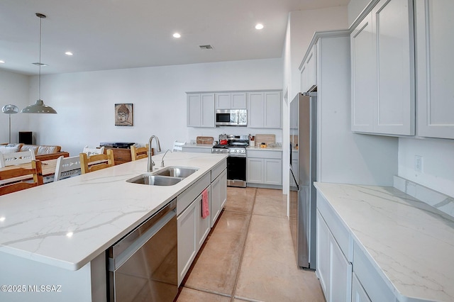 kitchen featuring sink, hanging light fixtures, a center island with sink, appliances with stainless steel finishes, and light stone countertops