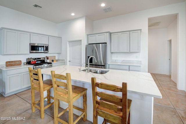 kitchen featuring sink, appliances with stainless steel finishes, gray cabinetry, an island with sink, and a kitchen bar