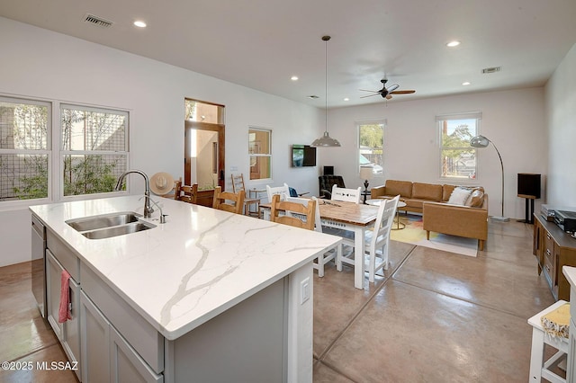 kitchen with sink, decorative light fixtures, a center island with sink, dishwasher, and light stone countertops