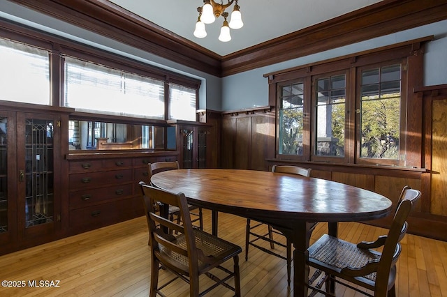 dining room with an inviting chandelier, ornamental molding, and light wood-type flooring