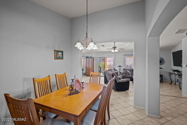 tiled dining room featuring ceiling fan with notable chandelier and a towering ceiling