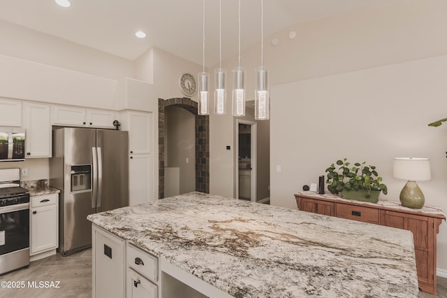 kitchen with vaulted ceiling, appliances with stainless steel finishes, decorative light fixtures, white cabinetry, and light stone countertops