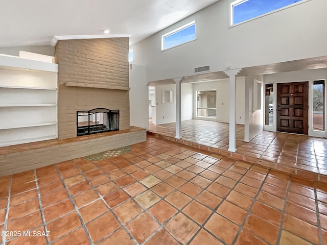 unfurnished living room featuring high vaulted ceiling, tile patterned flooring, visible vents, a brick fireplace, and ornate columns