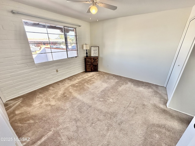 spare room with carpet, ceiling fan, and brick wall