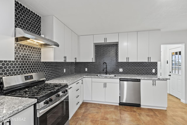 kitchen featuring appliances with stainless steel finishes, sink, white cabinets, light stone countertops, and wall chimney range hood