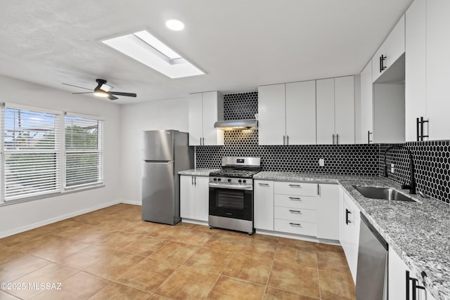 kitchen featuring range hood, a skylight, a sink, decorative backsplash, and appliances with stainless steel finishes