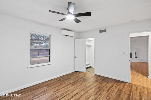 unfurnished bedroom with visible vents, a ceiling fan, a wall mounted AC, wood finished floors, and baseboards
