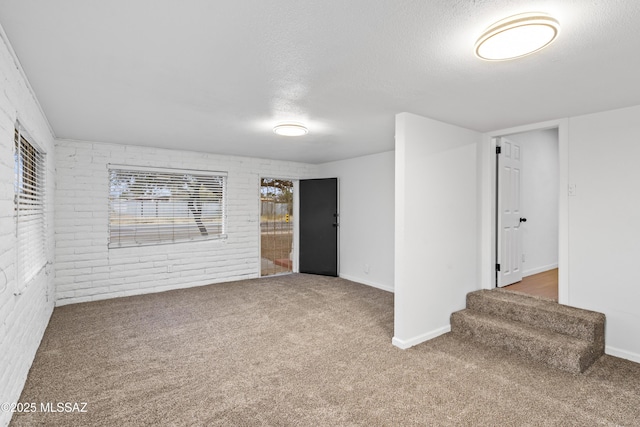 unfurnished room featuring brick wall, baseboards, carpet, stairway, and a textured ceiling