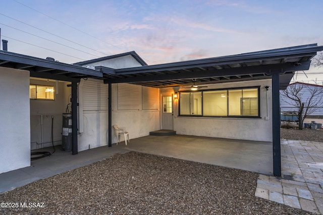 back of house at dusk with stucco siding, a patio, and fence
