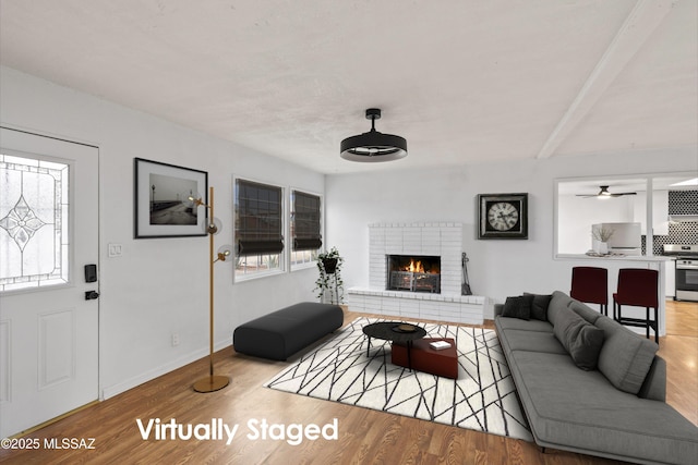 living room with a healthy amount of sunlight, a brick fireplace, baseboards, and wood finished floors