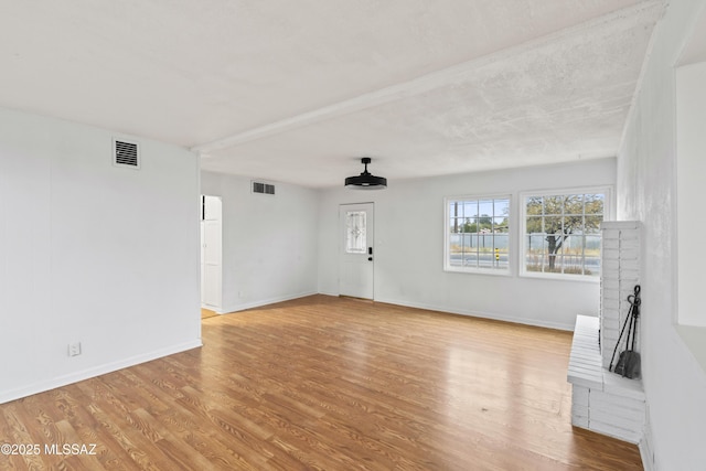 unfurnished living room with wood finished floors, visible vents, and baseboards