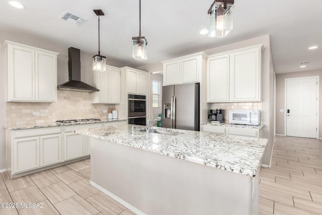 kitchen featuring stainless steel appliances, a center island with sink, wall chimney range hood, and white cabinets