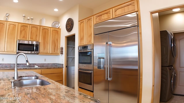 kitchen with light stone counters, stainless steel appliances, sink, and stacked washer / drying machine