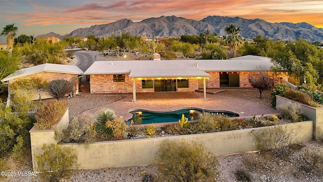 back house at dusk featuring a mountain view and a patio area