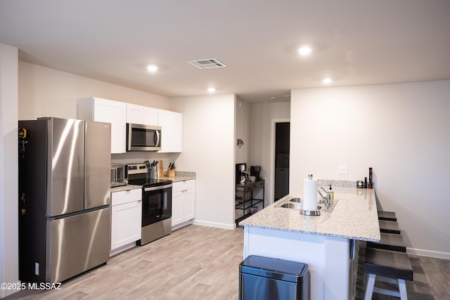 kitchen featuring visible vents, a breakfast bar area, a peninsula, stainless steel appliances, and a sink