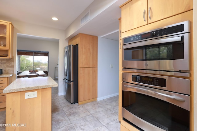 kitchen featuring light brown cabinetry, tasteful backsplash, stainless steel appliances, and light tile patterned flooring