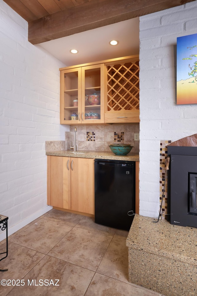 bar with light brown cabinetry, light stone counters, fridge, brick wall, and beam ceiling