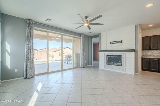 unfurnished living room featuring a tiled fireplace, light tile patterned flooring, and ceiling fan