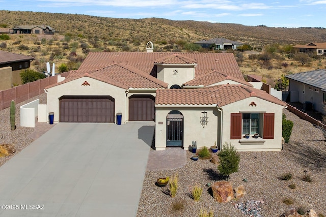 mediterranean / spanish-style house with an attached garage, fence, a tiled roof, concrete driveway, and stucco siding