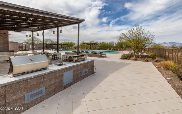 view of patio with an outdoor kitchen, fence, and a community pool