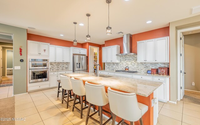 kitchen featuring light tile patterned flooring, appliances with stainless steel finishes, wall chimney exhaust hood, and a sink
