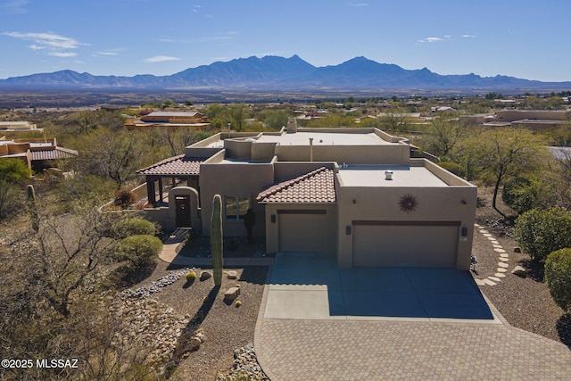 pueblo revival-style home with a garage, a mountain view, concrete driveway, and stucco siding