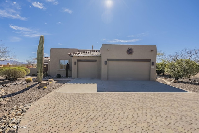 pueblo-style house featuring a garage, decorative driveway, a tiled roof, and stucco siding