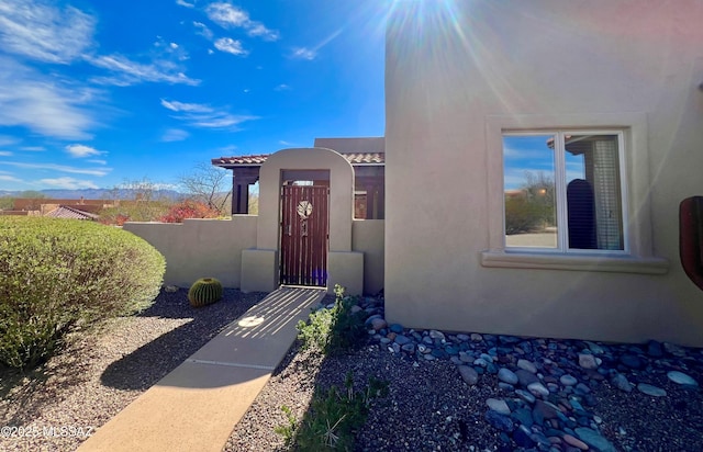 entrance to property featuring a tile roof, fence, and stucco siding