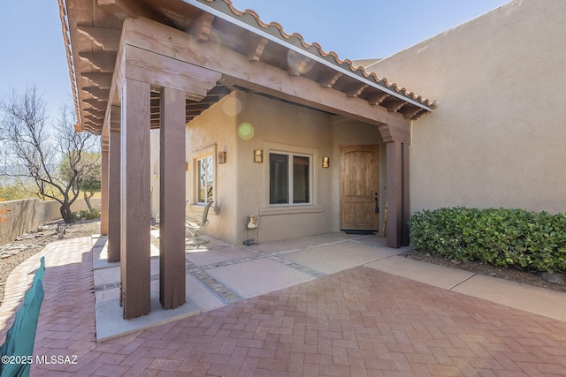 doorway to property featuring a tile roof, stucco siding, fence, and a patio