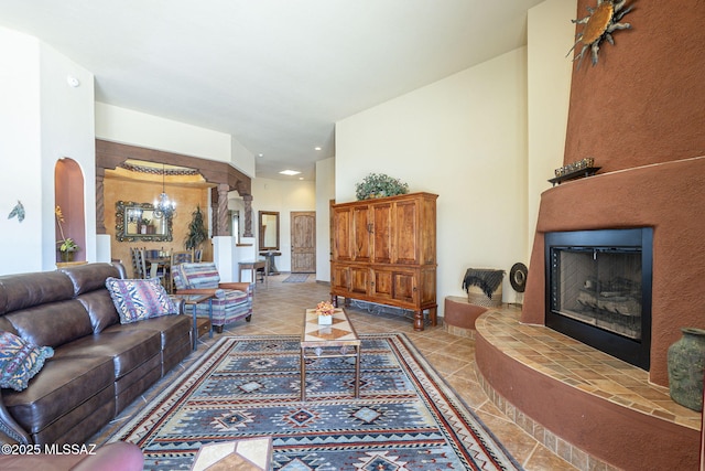 living area featuring decorative columns, arched walkways, a fireplace with raised hearth, and tile patterned floors