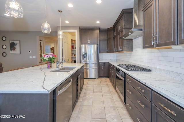 kitchen with appliances with stainless steel finishes, a sink, wall chimney range hood, dark brown cabinets, and light stone countertops