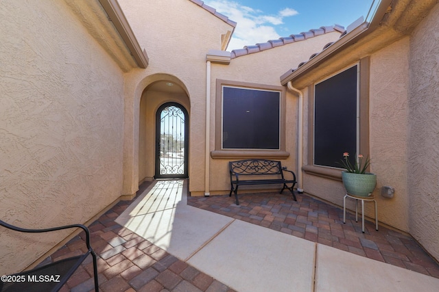 doorway to property featuring a tile roof, a patio, and stucco siding