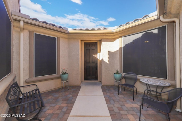 doorway to property with a patio area, a tiled roof, and stucco siding