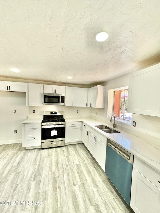 kitchen featuring white cabinets, appliances with stainless steel finishes, a textured ceiling, light wood-type flooring, and a sink