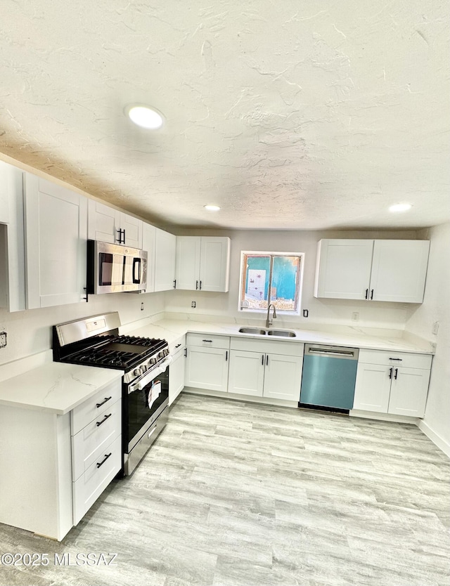 kitchen with a sink, white cabinets, appliances with stainless steel finishes, light wood-type flooring, and light stone countertops