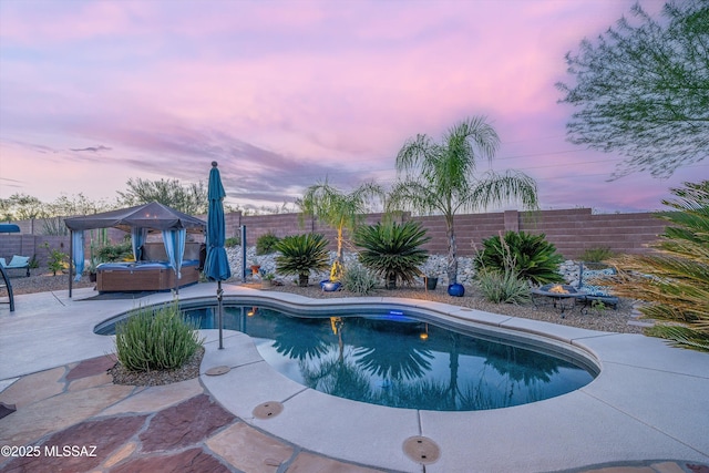 pool at dusk featuring a hot tub, a gazebo, and a patio