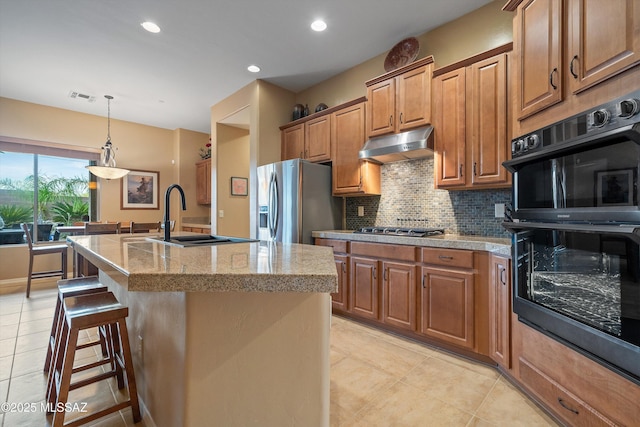 kitchen with sink, a breakfast bar area, stainless steel appliances, tasteful backsplash, and an island with sink