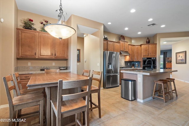 kitchen featuring appliances with stainless steel finishes, decorative light fixtures, tasteful backsplash, a breakfast bar area, and a center island with sink