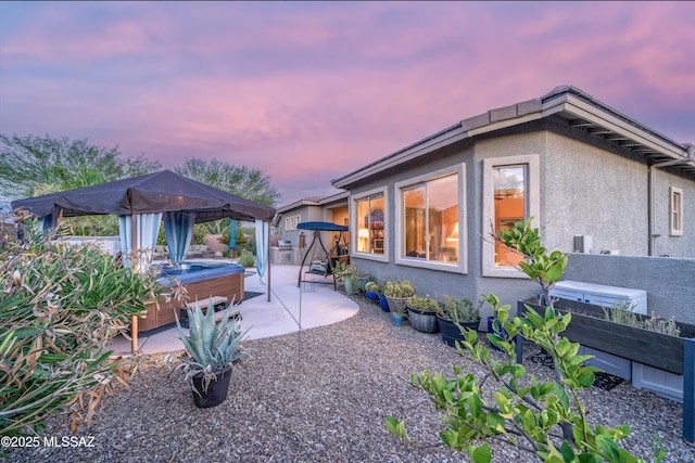 patio terrace at dusk featuring a hot tub and a gazebo