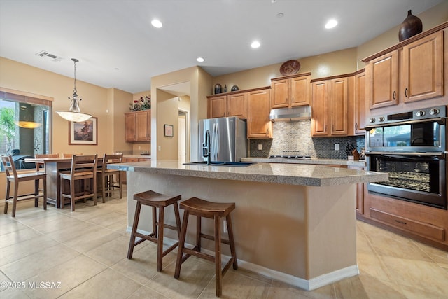 kitchen featuring sink, hanging light fixtures, stainless steel appliances, tasteful backsplash, and a center island with sink