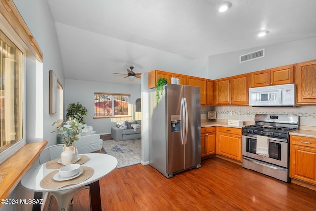 kitchen with lofted ceiling, appliances with stainless steel finishes, ceiling fan, hardwood / wood-style floors, and backsplash