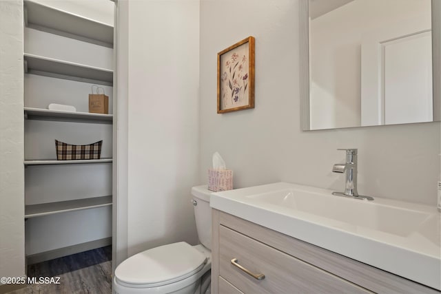 half bathroom featuring toilet, vanity, a closet, and wood finished floors