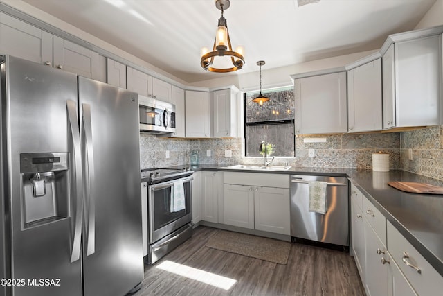 kitchen featuring pendant lighting, dark wood finished floors, dark countertops, backsplash, and appliances with stainless steel finishes