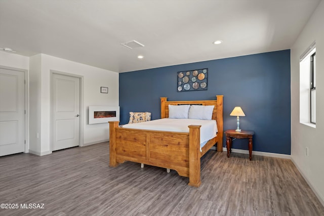 bedroom featuring dark wood-style flooring, recessed lighting, visible vents, a warm lit fireplace, and baseboards